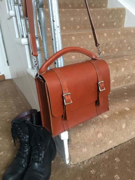 Leather A5 satchel shoulder bag hanging a foot stairs next to black boots