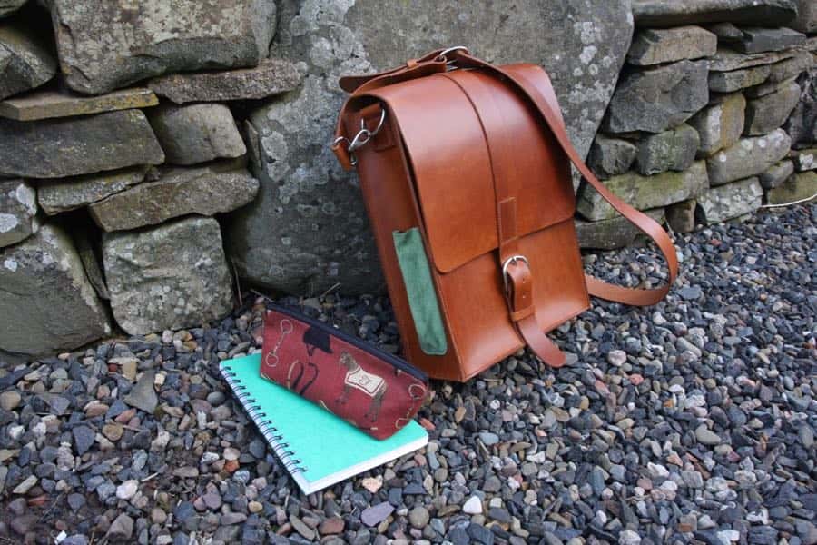 Leather messenger shoulder bag against a wall with pencil case for scale