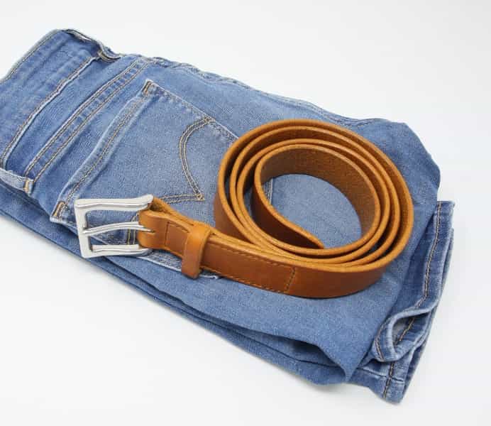 Italian tan leather belt with shiny nickel buckle shown own a pair of jeans.