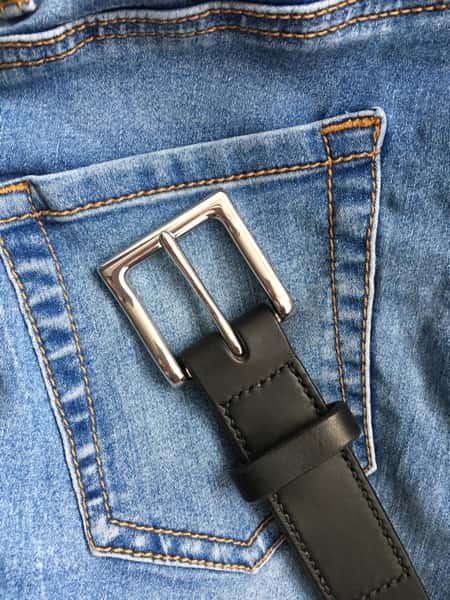 Italian black leather belt with silver buckle shown against blue jeans
