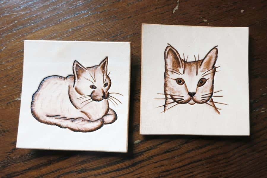 Pair of cat motif square leather drinks coasters on a dark wood background